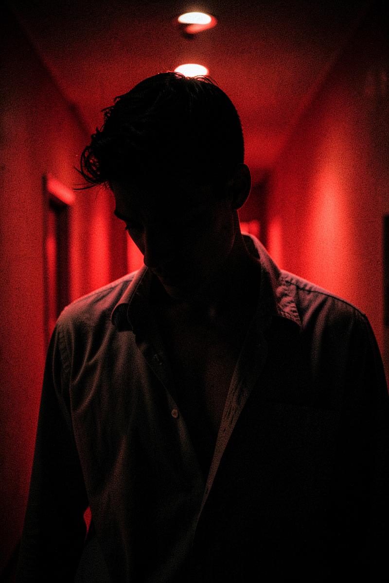 Dossier portrait slot: a young man backlit in a red-lit corridor.